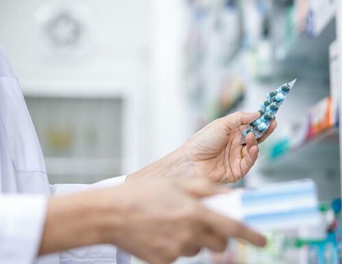 Apothekerin hält eine Blisterpackung mit blauen Kapseln in einer Apotheke